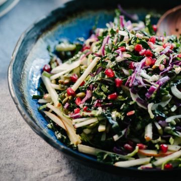 A kale pomegranate salad with apples, fennel, and pepitas in a blue ceramic bowl.
