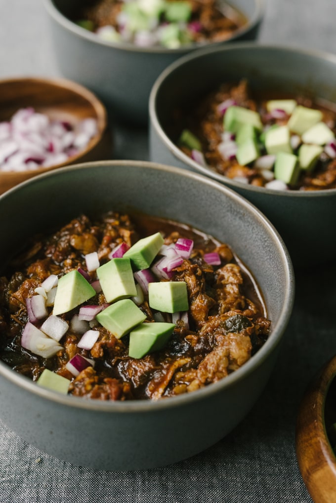 Several bowls of whole30 and paleo chili con carne on a grey tablecloth. 
