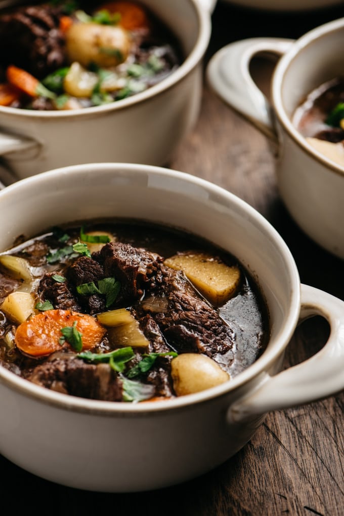 A bowl of dutch oven braised red wine beef stew on a wood table.