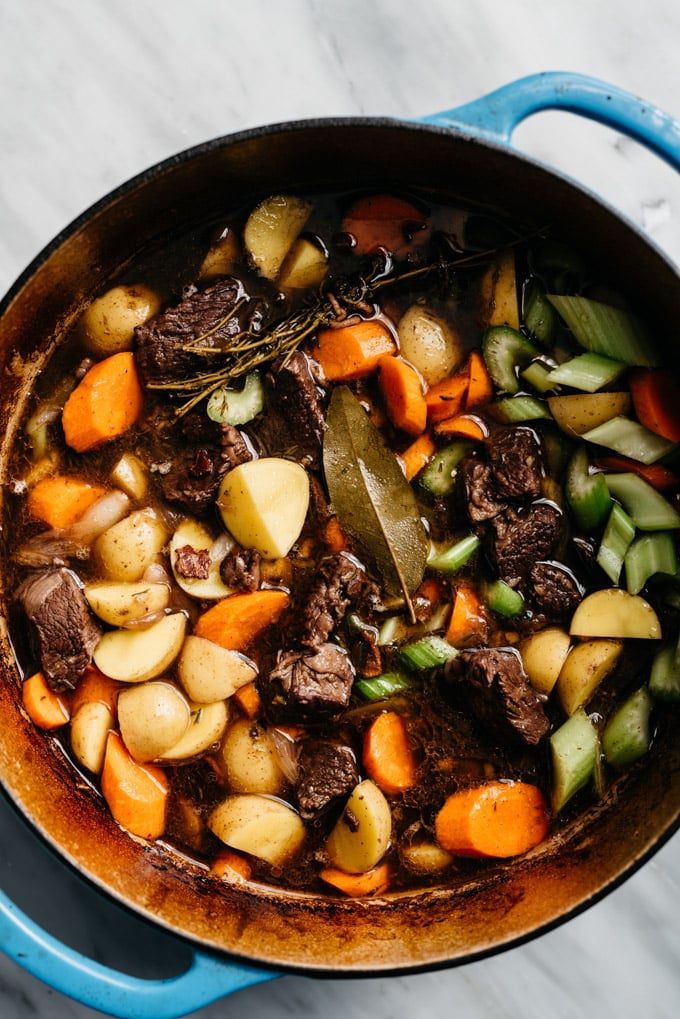 A dutch oven filled with beef braised in red wine with carrots, celery, and onion added to create an oven braised red wine beef stew.
