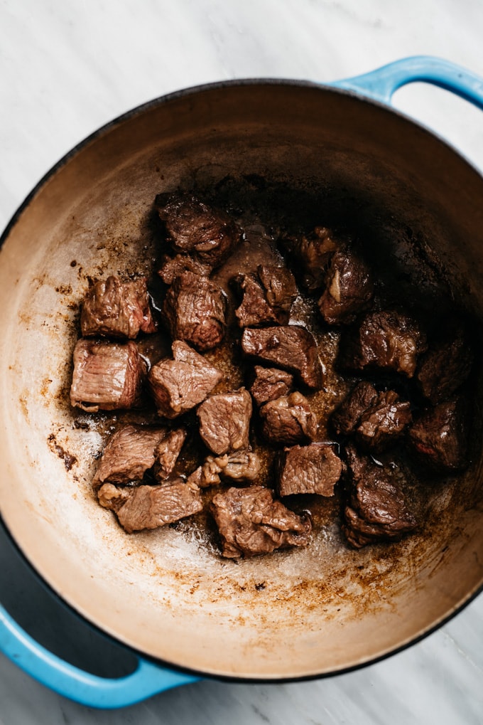 Cubes of beef chuck roast browning in a dutch oven for a red wine beef stew recipe.