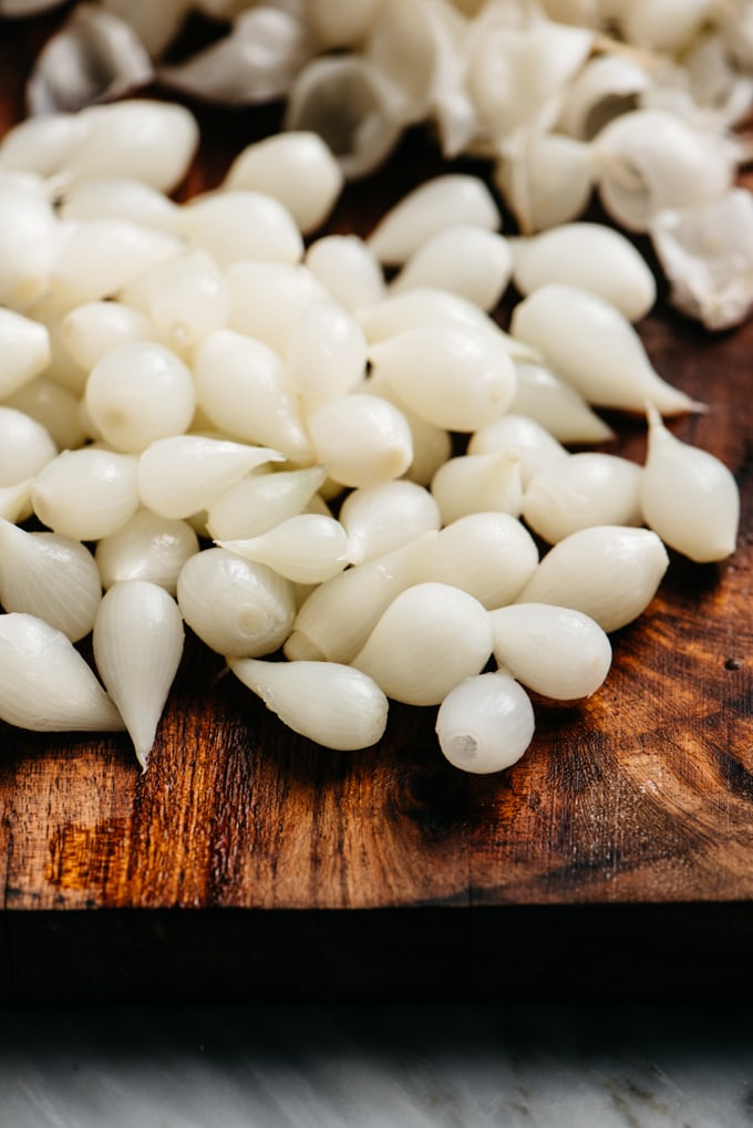 Peeled pearl onions on a cutting board for adding to red wine beef stew.
