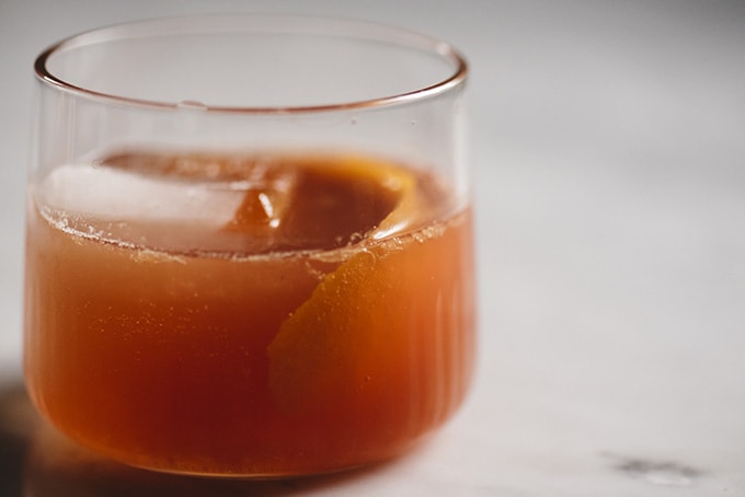 An old fashioned cocktail in a rocks glass poured over a giant ice cube with an orange peel garnish.