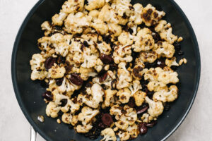 Roasted cauliflower in a skillet tossed with olives, raisins, and pine nuts.