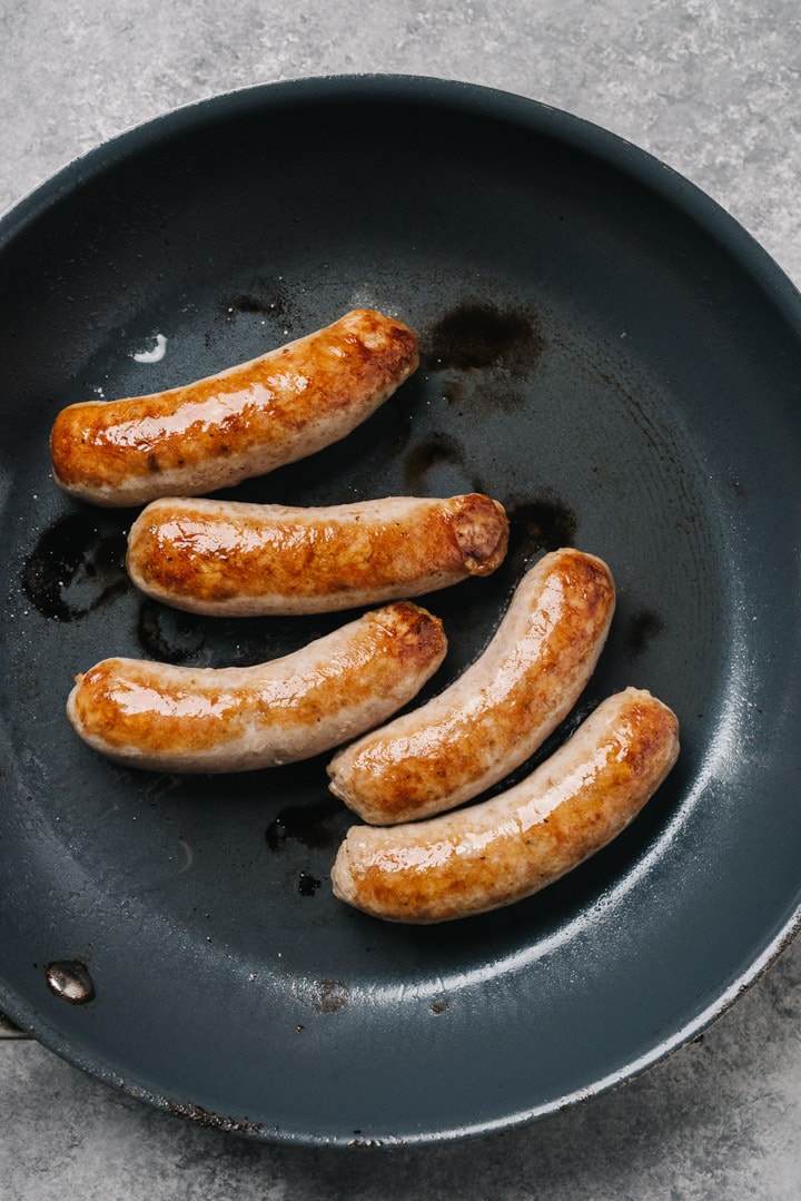 Italian sausage links browning in a skillet.