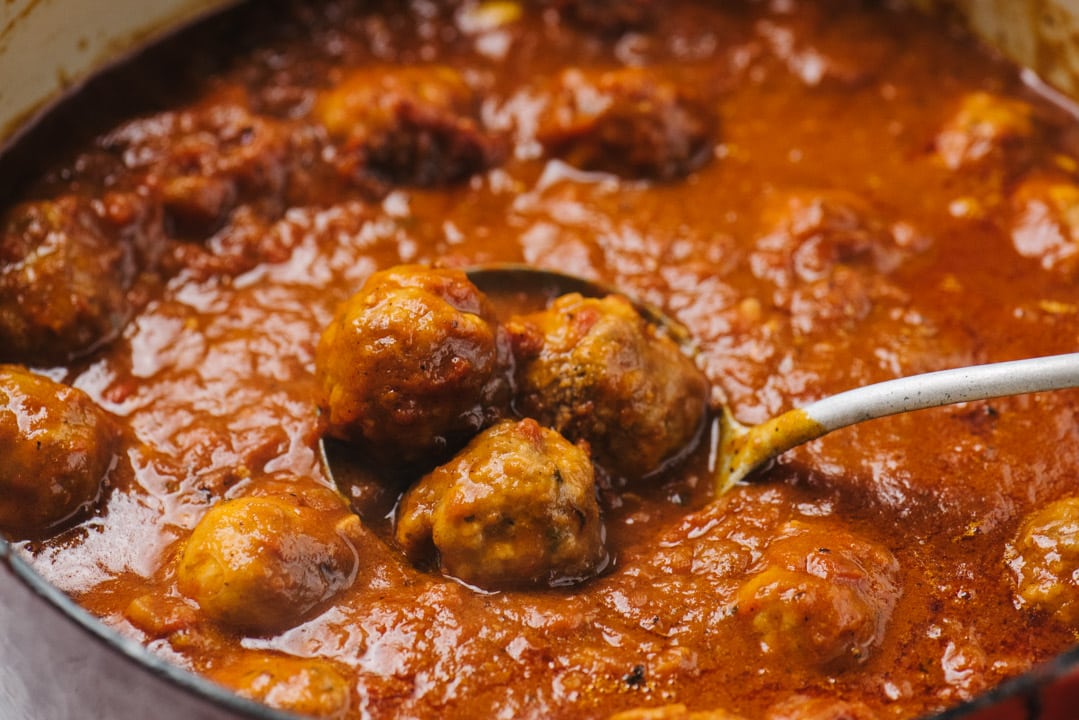 A ladle dipped into sunday gravy with meatballs and italian sausage.