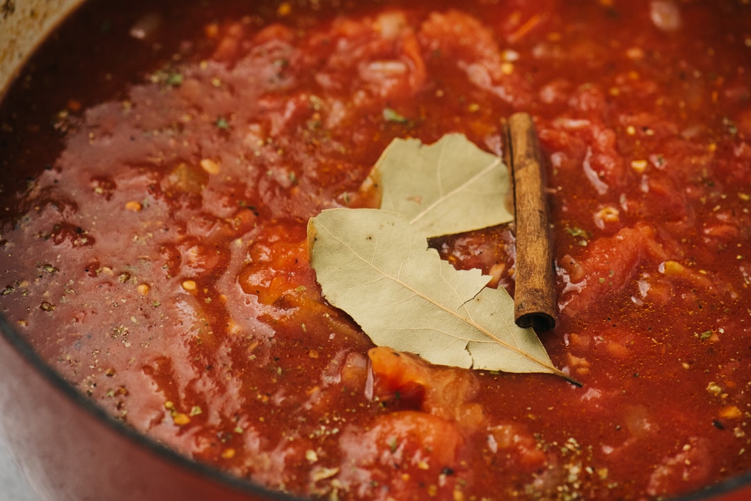 Sunday sauce in a dutch oven topped with bay leaves and a cinnamon stick before simmering.