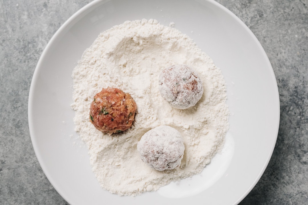 Meatballs dusted with flour in a shallow white bowl.