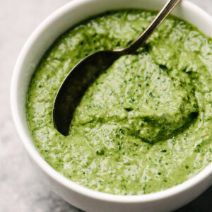 Side view, a spoon dipped into a bowl of creamy spinach pesto sauce.
