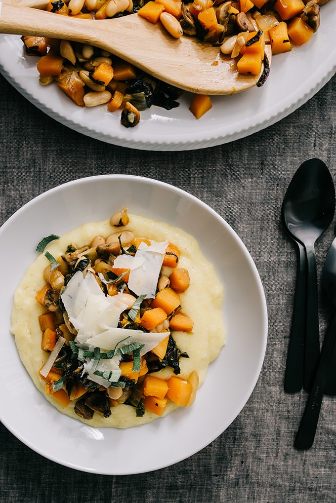 An image of an individual bowl of white bean ragout with butternut squash over cheesy polenta on a grey linen background. 