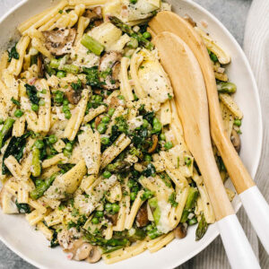 Spring pasta primavera in a large white pasta bowl with wood serving spoons.