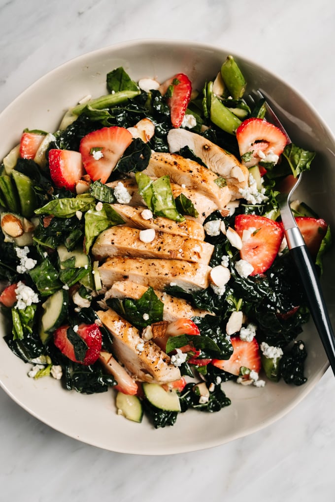 From above, strawberry kale salad in a shallow bowl topped with grilled chicken.