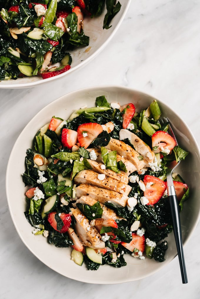 From above, strawberry kale salad in a shallow bowl topped with grilled chicken.