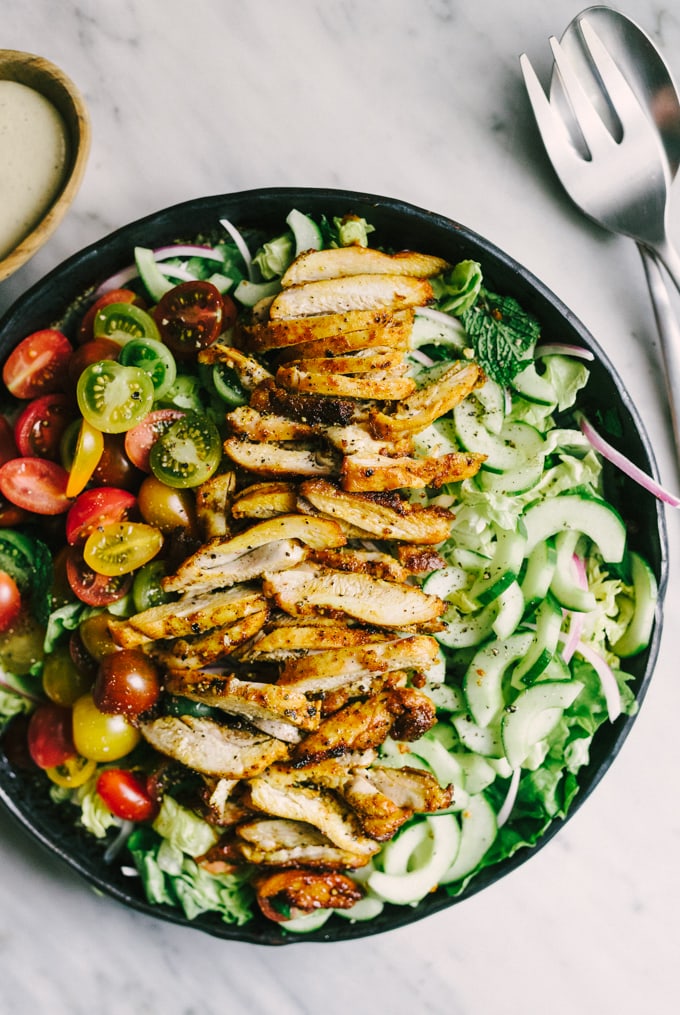 A bowl of fresh chicken shawarma salad - tender slices of marinated and oven baked chicken thighs, sliced cucumbers, and fresh tomatoes on a bed of lettuce, parsley, and mint. 