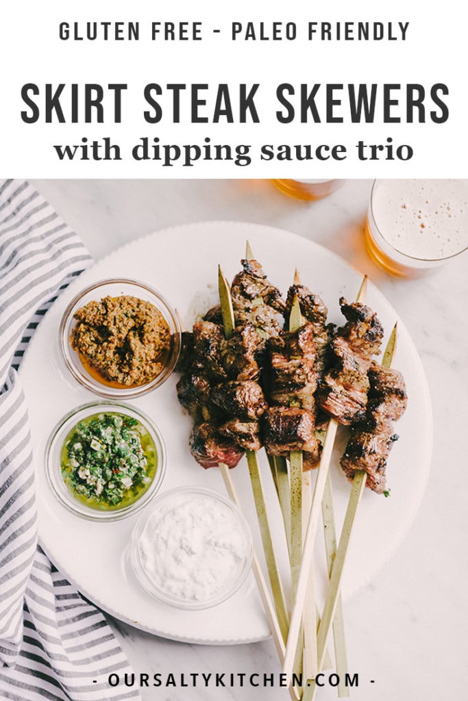 Skirt steak skewers on a white serving platter with three bowls of dipping sauces.