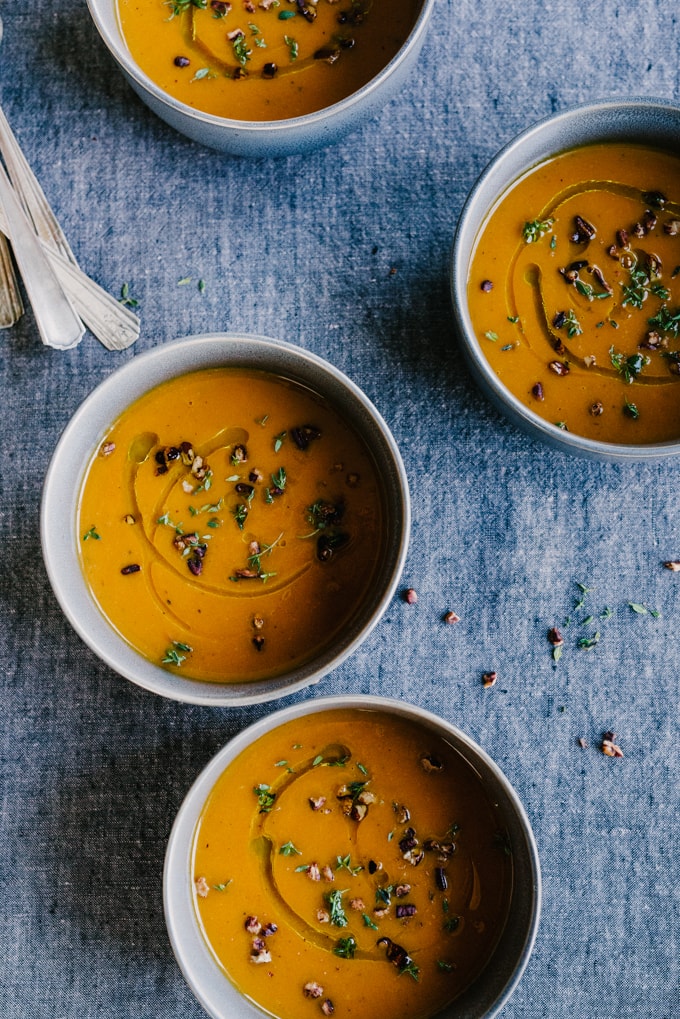 Four bowls of roasted carrot apple soup on a blue tablecloth.