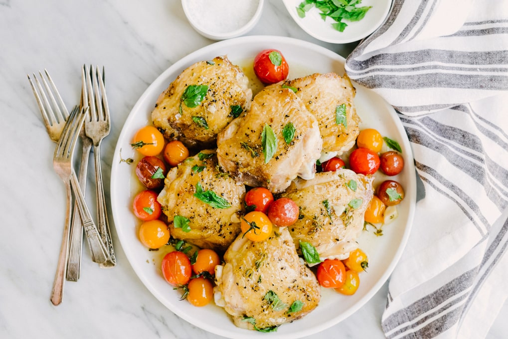 These crispy chicken thighs are whole foods family favorite. Crispy chicken skin, juicy thigh meat, and sweet tomatoes that burst with a satisfying little "pop". This is an easy, tasty, real food recipe that's on the table in just about 35 minutes. A winning weeknight dinner! #paleo #wholefood #realfood #whole30 