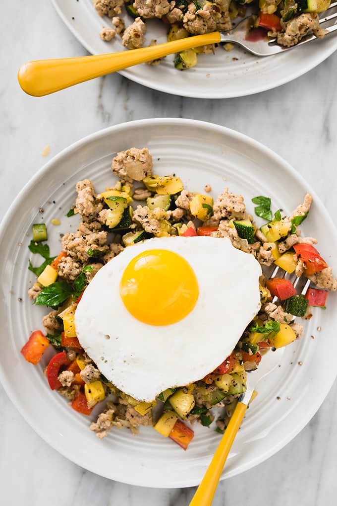 A grey plate filled with ground turkey hash and topped with a fried egg - and easy and flexible summer paleo recipe.