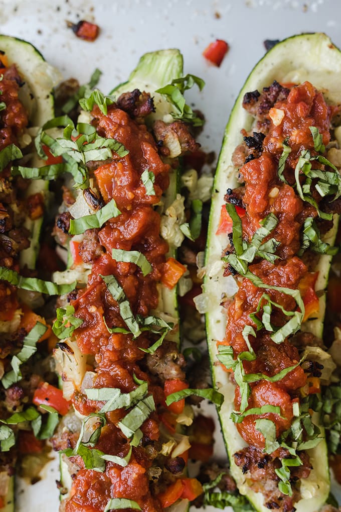 An easy summer paleo recipe - three zucchini halves stuffed with italian sausage, vegetables, and fresh marinara, then topped with basil.