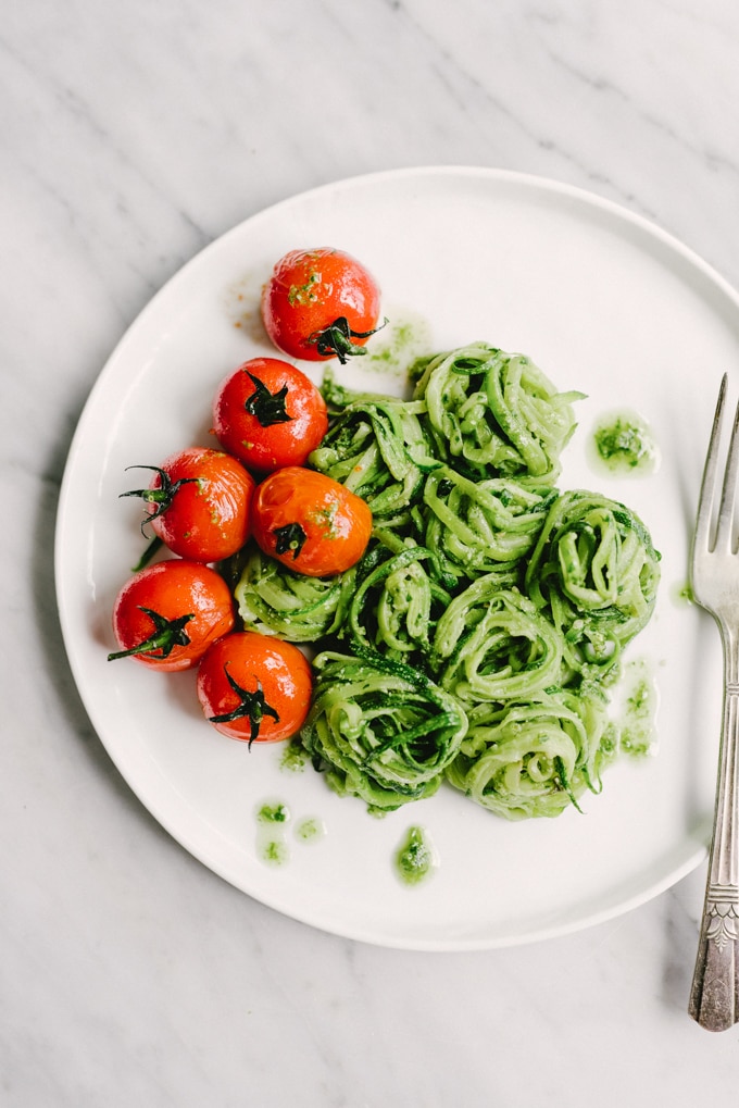 Summer tarragon pesto tossed with zucchini noodles and burst tomatoes on a white plate - an easy and elegant vegan and paleo summer recipe. 
