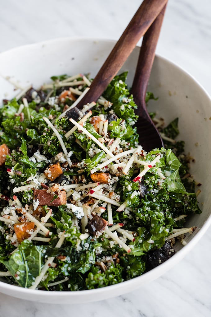 A large white salad bowl on a marble table filled with the base of a kale chicken salad tossed with maple cider vinaigrette. 