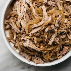 Slow cooker apple cider pulled pork in a white serving bowl on a marble table.