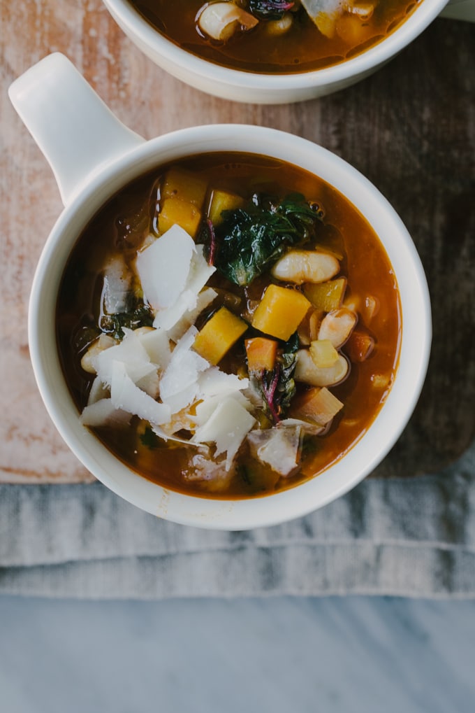 A crock of gluten free winter minestrone soup recipe packed with healthy, nutritious vegetables resting on a wood cutting board. 