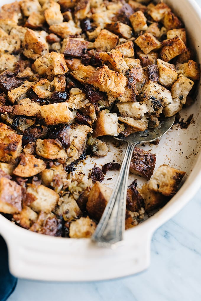 A casserole dish filled with baked sausage and cranberry stuffing with one portion missing and a serving spoon. 