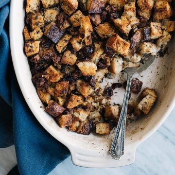 A casserole dish of sausage and cranberry stuffing with rye bread croutons with a blue linen napkin.