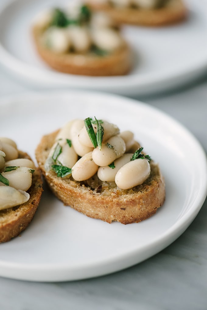 These rosemary marinated white bean bruschetta are a fast, easy, healthy and insanely delicious holiday party appetizer. They can be almost entirely prepared in advance, hold up well at room temperature, and size up easily for a crowd. The perfect party appetizer recipe! #appetizer #vegan #vegetarian #holidayparty #whitebeanbruschetta