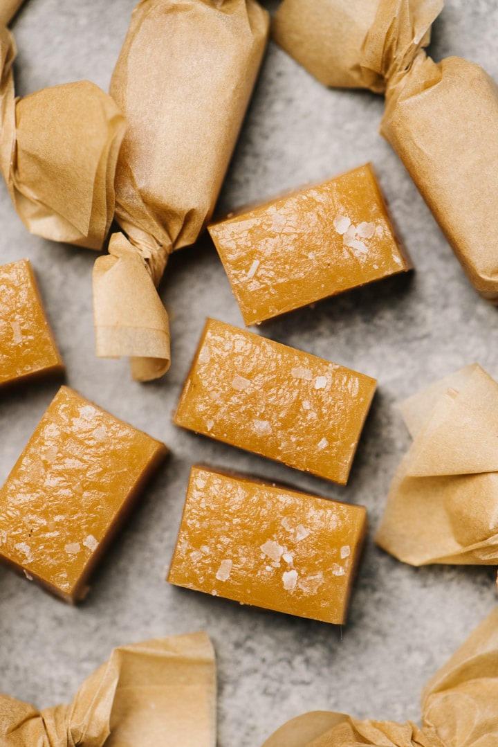 Several wrapped and unwrapped caramel candies on a concrete background.