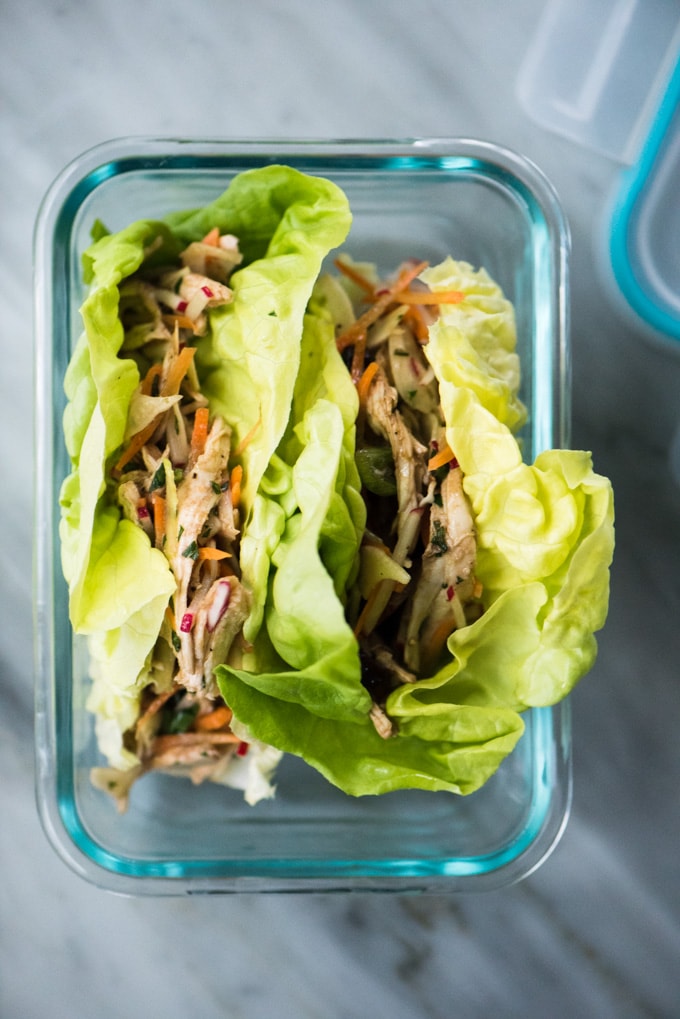 An overhead view of a glass lunchbox container filled with two paleo and whole30 chicken salad wraps. 