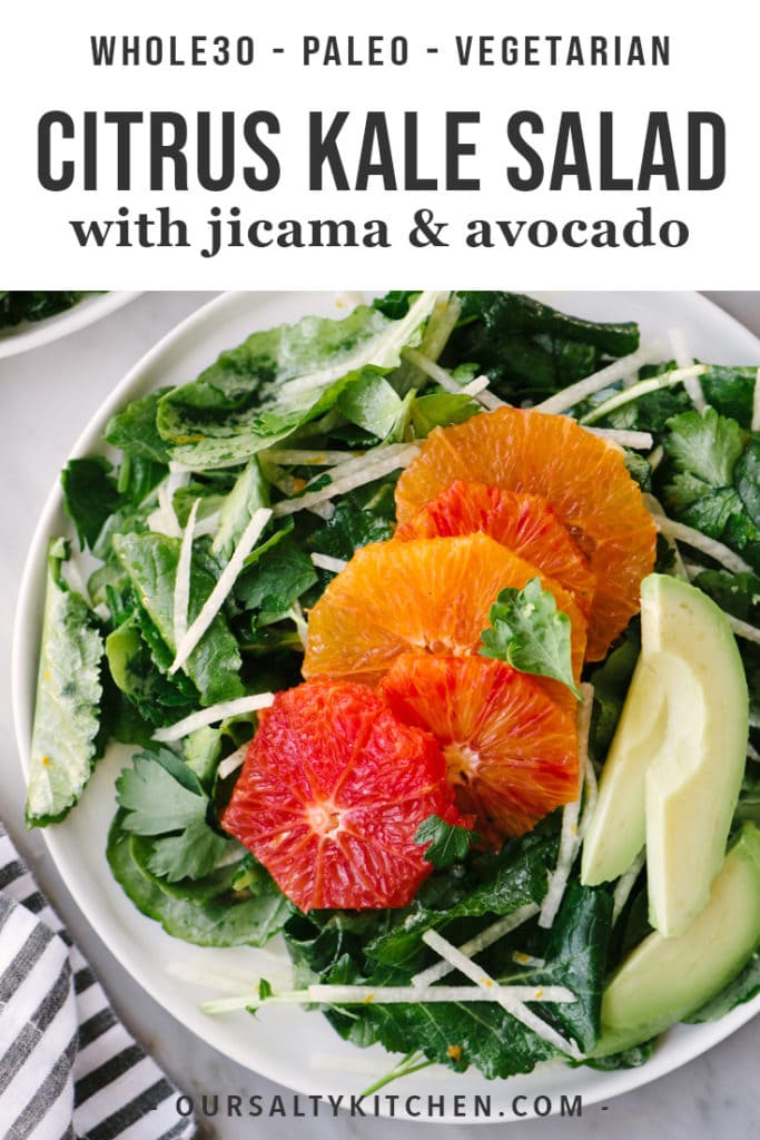 A plate of kale citrus salad with jicama and avocado on a marble table.