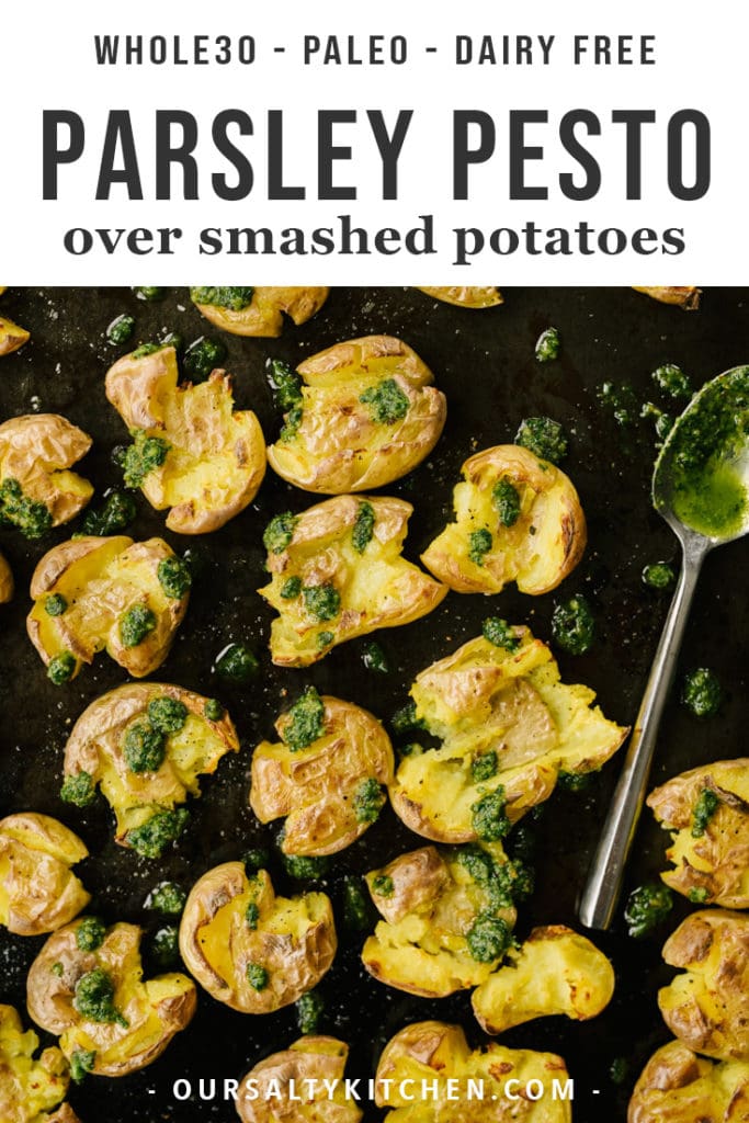 Crispy smashed potatoes on a baking sheet drizzled with dairy free and paleo parsley pesto.