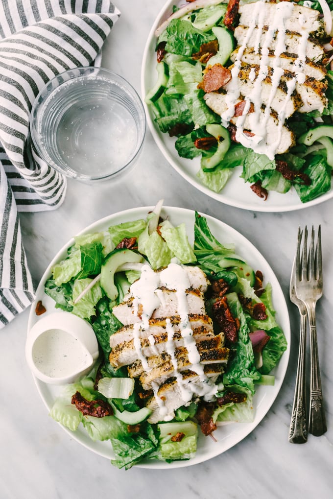 Two BLT chicken salads drizzled with Whole30 range dressing on a marble table with a striped napkin.