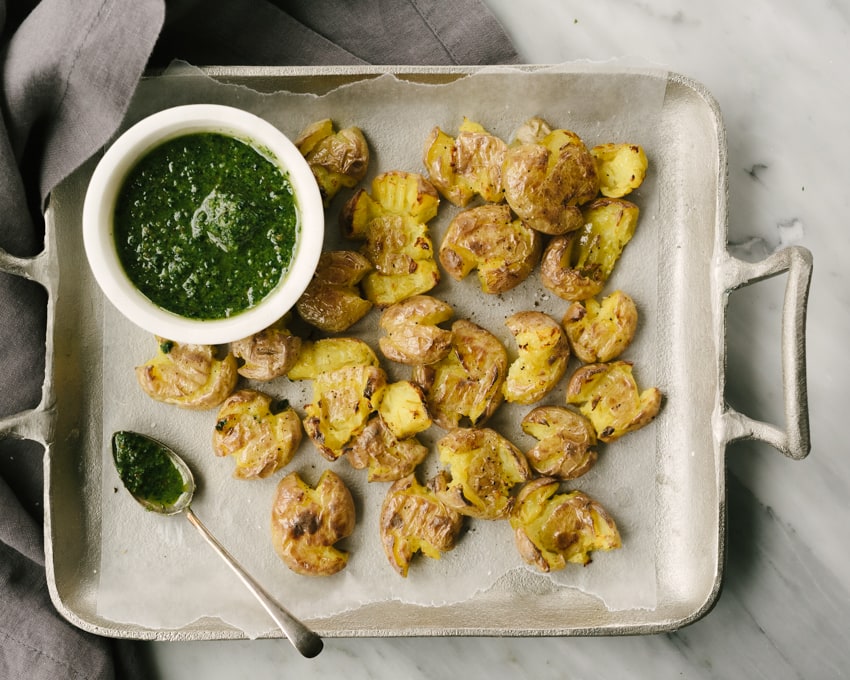 A platter filled with crispy smashed potatoes and a small bowl of paleo pesto dipping sauce. 