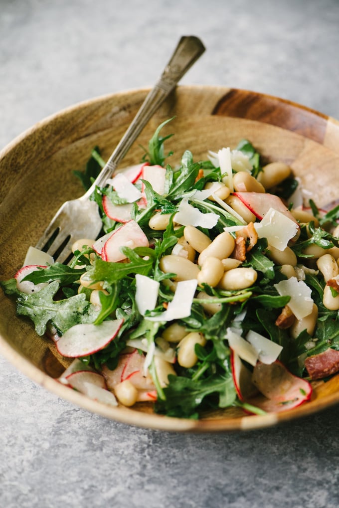 Marinated white bean salad with radishes, bacon, and arugula in a wooden salad bowl.