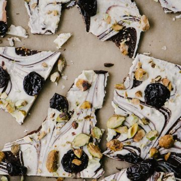 Pieces of white and dark chocolate bark with cherries and pistachios on a piece of parchment paper.