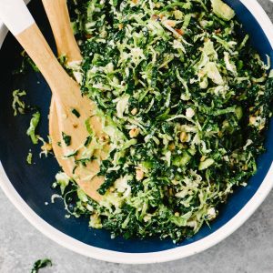 A bowl of shredded kale and brussels sprouts salad tossed with hazelnut vinaigrette in a blue and white bowl.