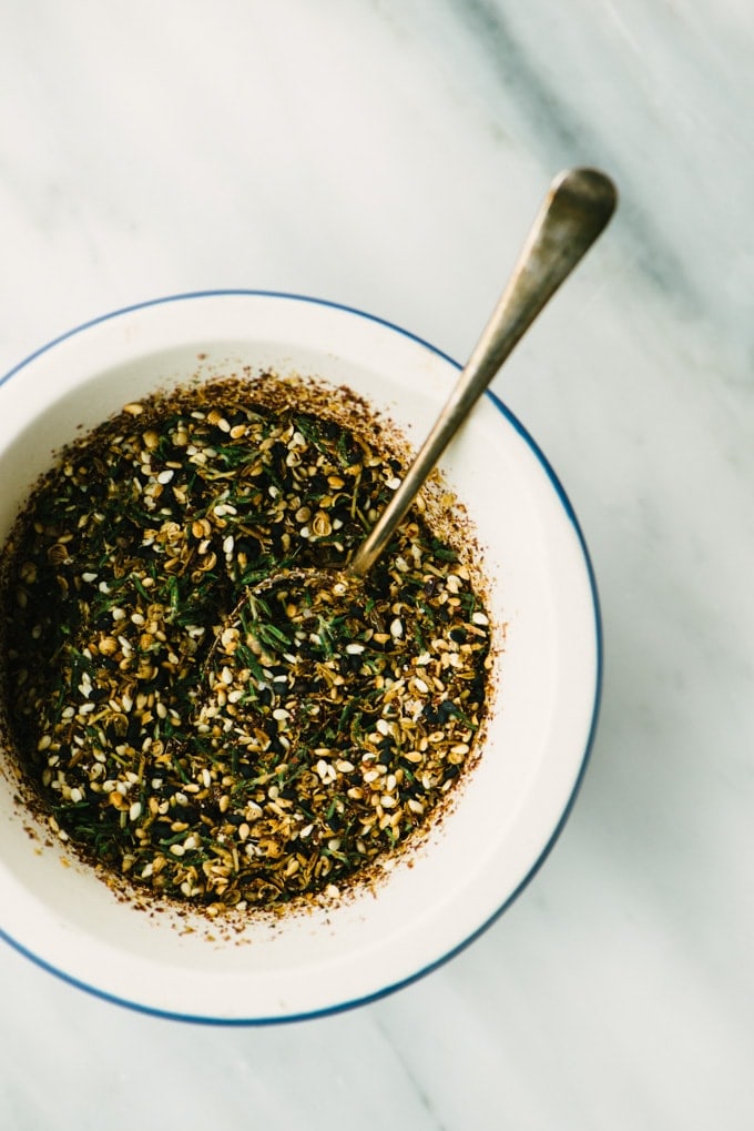 A recipe for homemade za'atar spice in a small bowl with a spoon on a marble table. 