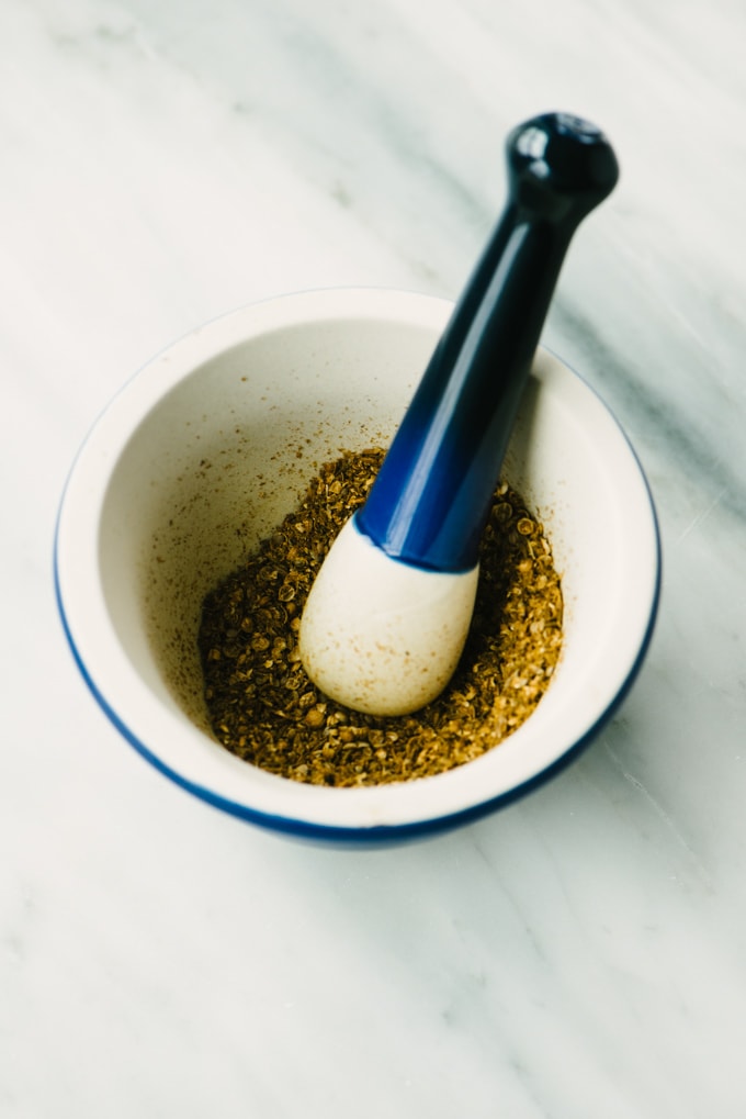 Whole cumin and coriander seeds ground with a pestle in a mortar for homemade za'atar.