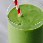 Mango spinach green smoothie in a glass with a red and white striped straw.