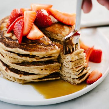 A stack of whole grain pancakes topped with macerated strawberries.