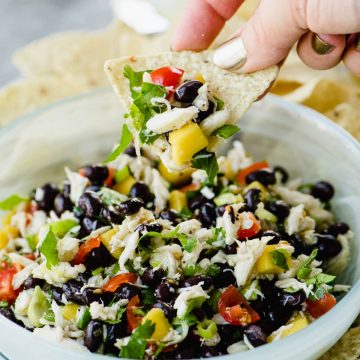 A woman dipping a tortilla chip into a bowl of black bean salsa with mango and lump crab meat.