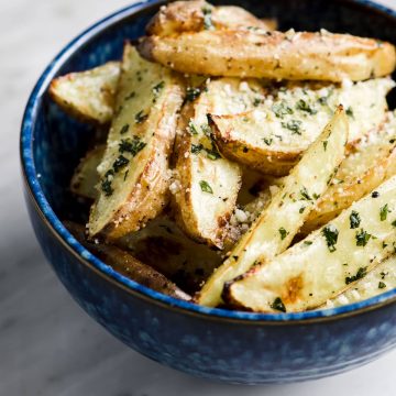 A bowl of crispy oven baked basil fries in a blue bowl on a marble table.