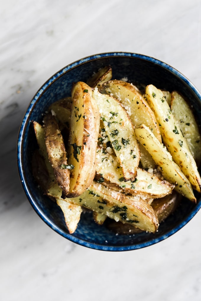A bowl of crispy baked potato wedge oven fries tossed with basil garlic butter.