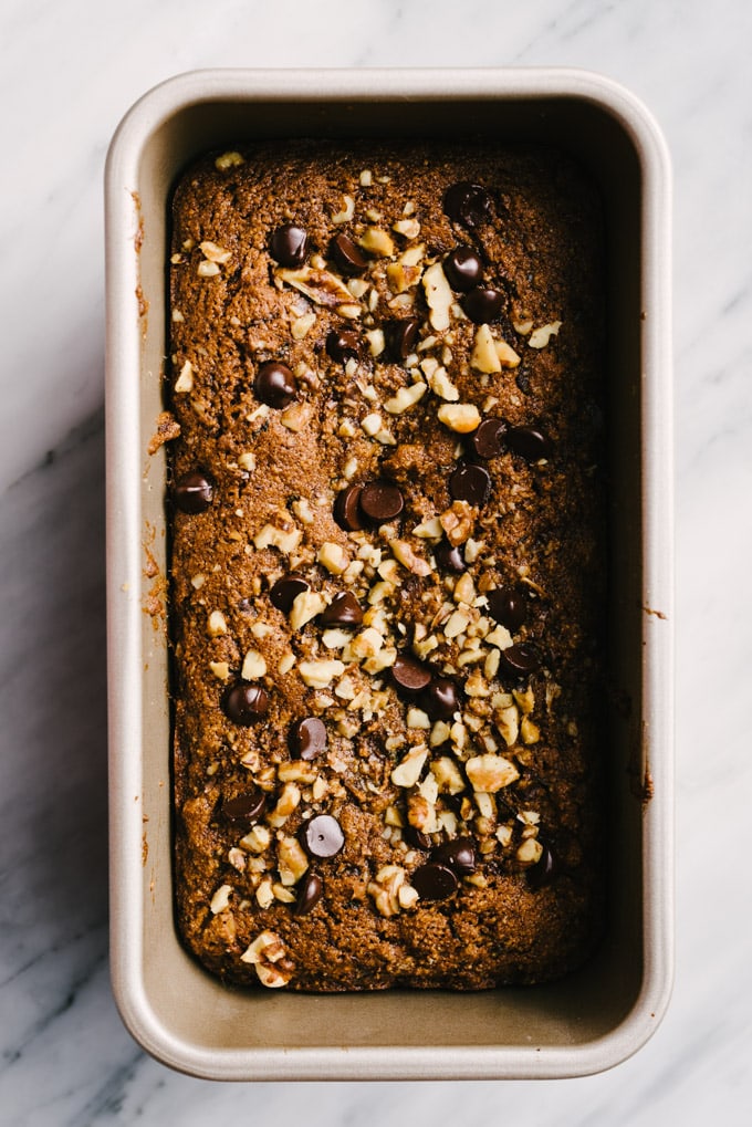 A loaf of paleo zucchini bread with almond flour and coconut oil, topped with walnuts and chocolate chips, fresh from the oven.