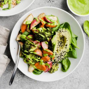 Roasted vegetable salad with raw spinach and avocado drizzled with green tahini dressing.