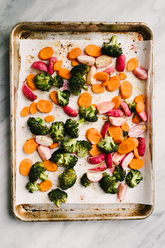 Broccoli florets, quartered radishes, and sliced carrots tossed with olive oil and spices on a parchment lined baking sheet.