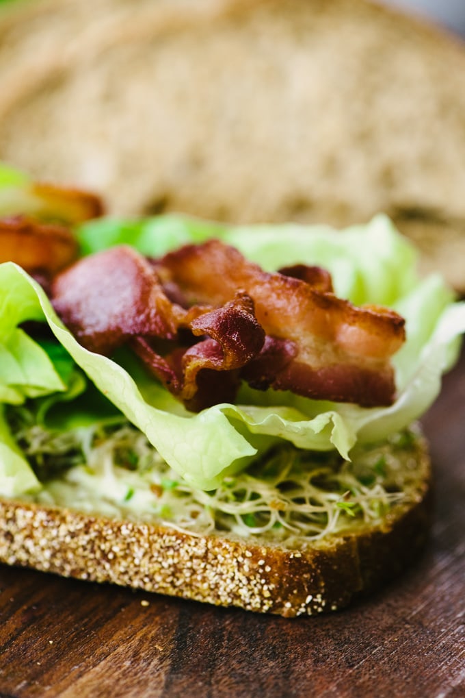 A slice of whole grain bread topped with garlic aioli, sprouts, butter lettuce, and bacon.